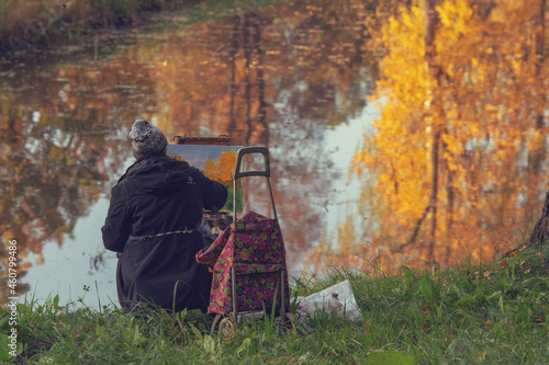 Pavlovsk, St Petersburg, Russia - October 3, 2021. An elderly woman artist paints an autumn landscape on the river bank. 