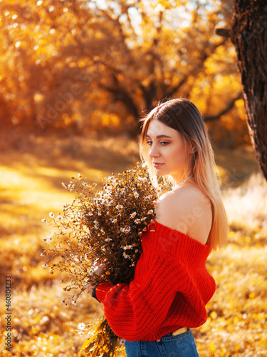 Outdoors atmospheric and sensual portrait of a young beautiful woman in a red warm sweater with a bouquet of daisies. Warm sunny autumn.