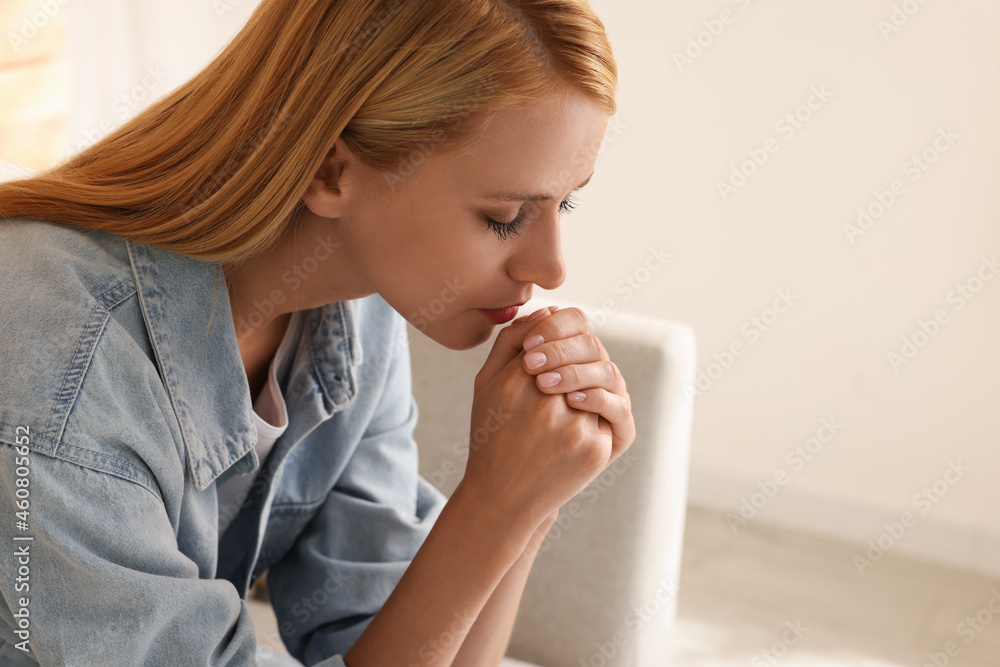 Religious young woman with clasped hands praying indoors. Space for text Religious young woman with clasped hands praying indoors. Space for text