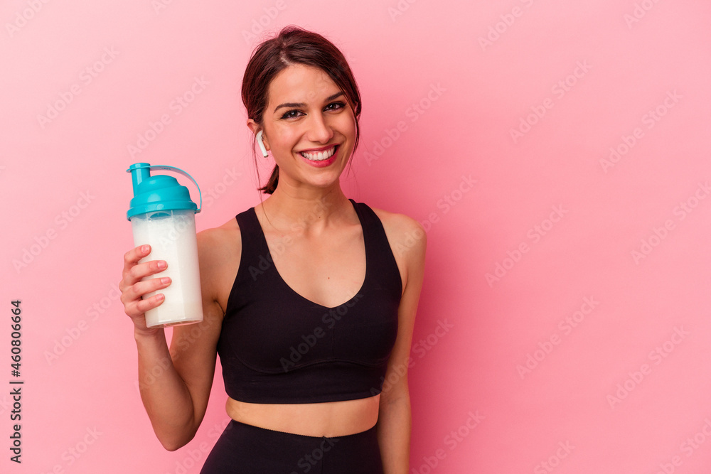 Young caucasian woman drinking a protein shake isolated on pink background