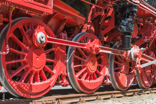 Fotografia Rote Räder und Antriebsstangen einer historischen Dampflokomotive auf Schienen,