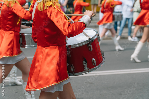 Young girls drummer in red vintage uniform at the parade. Street performance of festive march of drummers girls in red costumes on city street