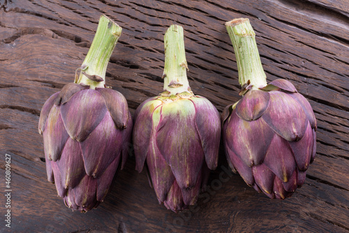 Green and purple artichoke flower edible buds on wooden background. photo