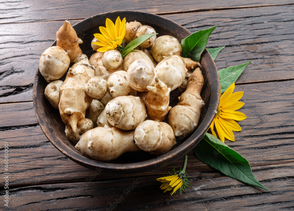 Jerusalem artichoke roots with leaves and flower of Jerusalem artichoke on a old wooden table.