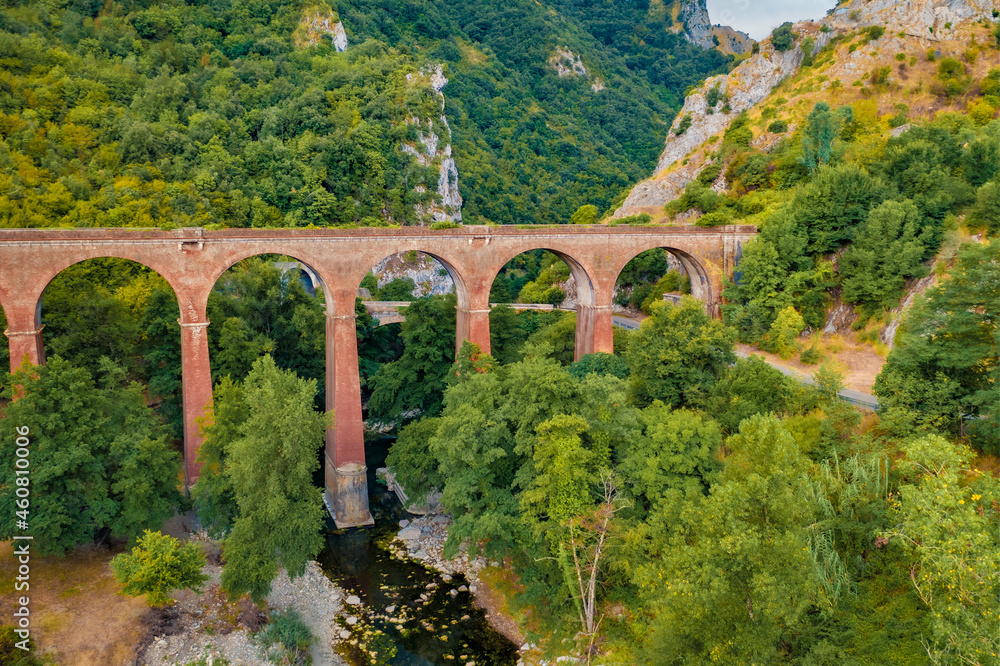 View from flying drone of ancient bridge across the Devil's Throat Gorge, San Severino village location. Aerial summer scene of Mingardo river, Italy, Europe. Traveling concept background.
