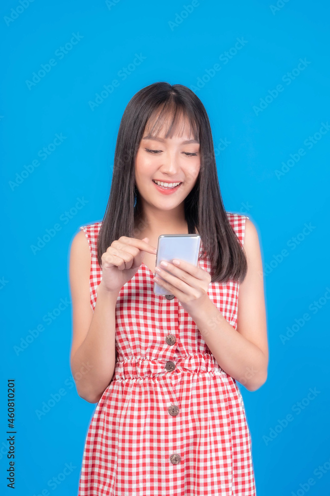 Beautiful Asian woman cute girl bangs hair style in red dress playing a smart phone isolated on blue background - mobile phone uses a online banking for pay online shopping Beautiful Asian woman cute girl bangs hair style in red dress playing a smart phone isolated on blue background - mobile phone uses a online banking for pay online shopping