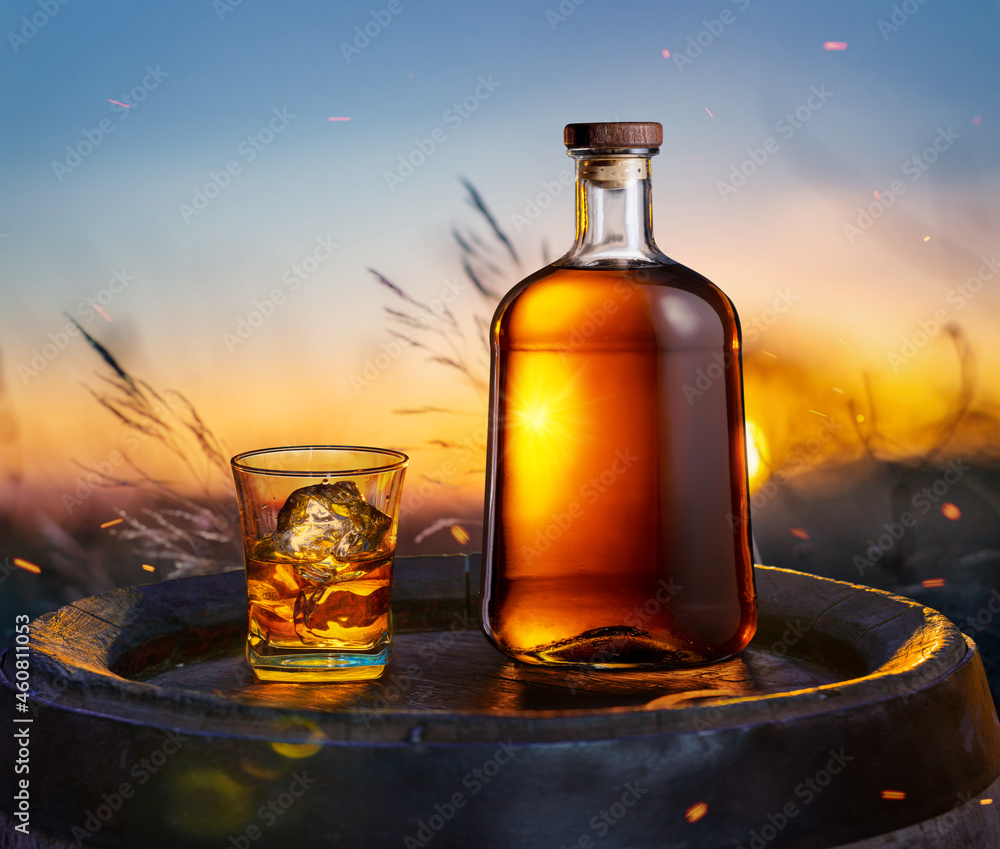 Carafe of whisky and glass of whisky on old wooden cask. Beautiful sunset at the background. Carafe of whisky and glass of whisky on old wooden cask. Beautiful sunset at the background.