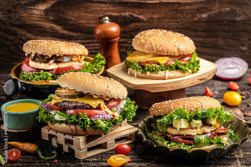 Tasty grilled homemade burgers with beef, tomato, cheese, bacon and lettuce on rustic wooden background. fast food and junk food concept
