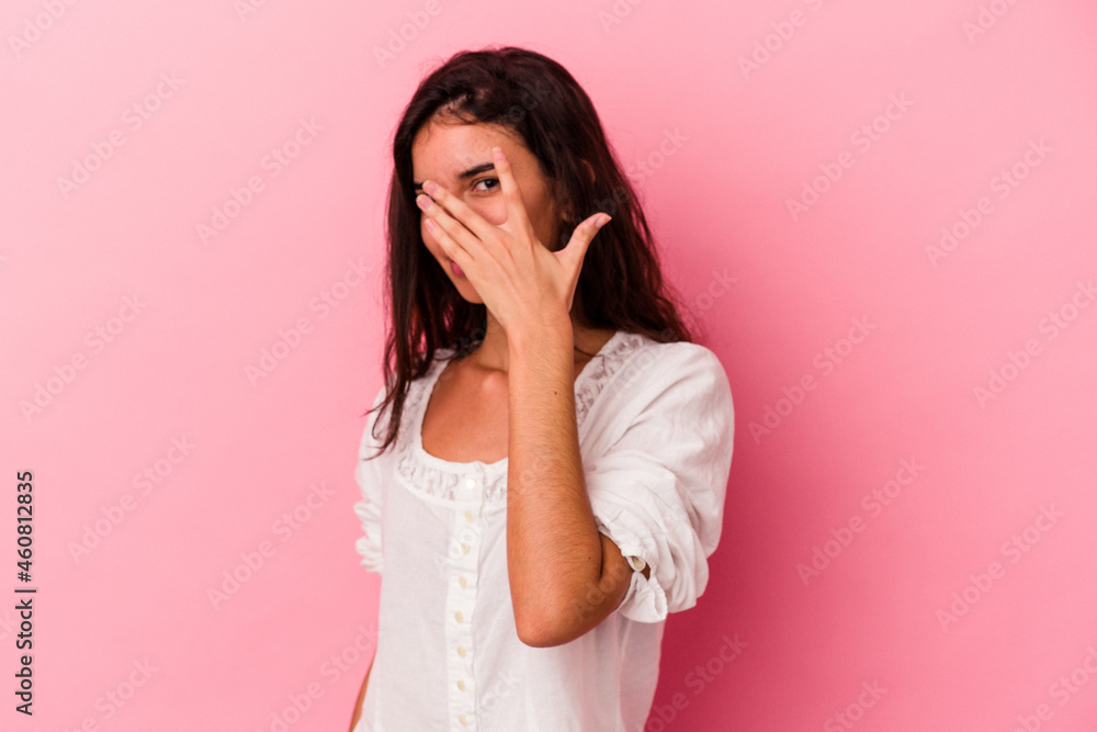 Young caucasian woman isolated on pink background blink at the camera through fingers, embarrassed covering face. Young caucasian woman isolated on pink background blink at the camera through fingers, embarrassed covering face.