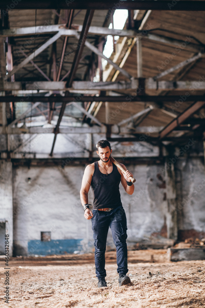 Strong Muscular Handsome Man in Black Tank Top with Baseball Bat Walksin Empty Grunge Hall
