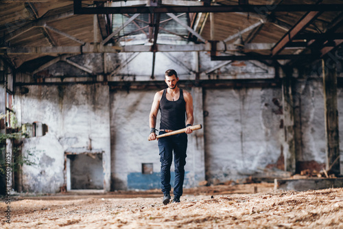 Strong Muscular Handsome Man in Black Tank Top with Baseball Bat Walksin Empty Grunge Hall 