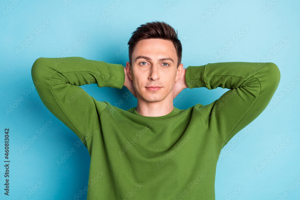 Photo of cool masculine guy hands behind head look camera wear green pullover isolated blue color background Photo of cool masculine guy hands behind head look camera wear green pullover isolated blue color background