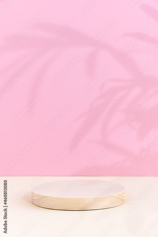 Minimal abstract background for the presentation of a cosmetic product. A cylindrical wooden scene on a beige table on a pink background. Premium podium with a shadow of tropical palm leaves on a pink