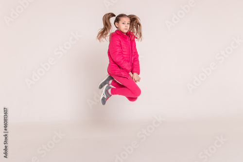a beautiful girl in a pink jacket jumps and smiles on a white background. happy childhood.