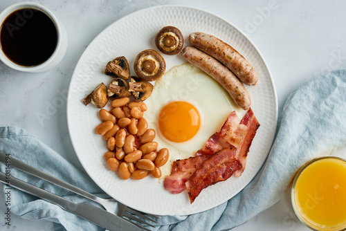 Traditional english breakfast with fried eggs, grilled sausages, roasted bacon, beans, mushrooms, coffee and orange juice. Typical british morning food. Keto diet meal. Horizontal, top view