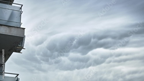 Time lapse of Mammatus Clouds near apartment balconies, on light gray sky. Weather, meteorology, urban, city.