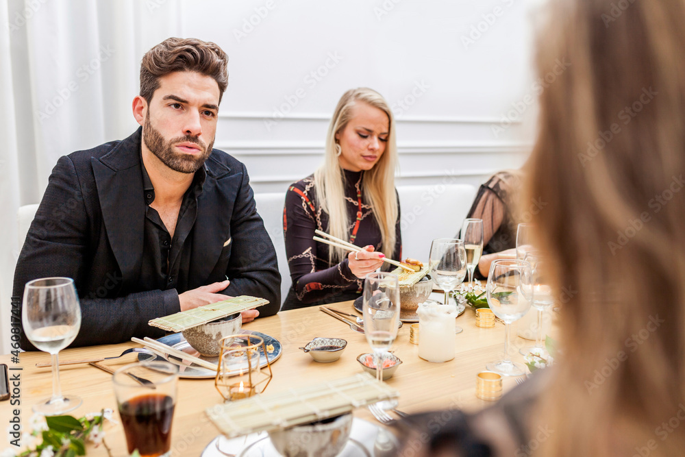 Group of friends conversating during dinner. Handsome man talking and eating sushi with female friends at a private dinner party. Group of friends conversating during dinner. Handsome man talking and eating sushi with female friends at a private dinner party.