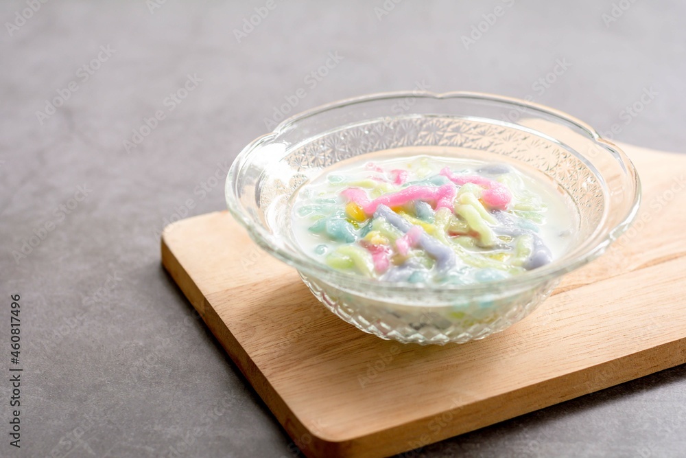 Thai dessert. Colorful of cendol with coconut milk in a clear bowl on a dark table. Delicious famous sweet dish in Thailand. Thai dessert. Colorful of cendol with coconut milk in a clear bowl on a dark table. Delicious famous sweet dish in Thailand.