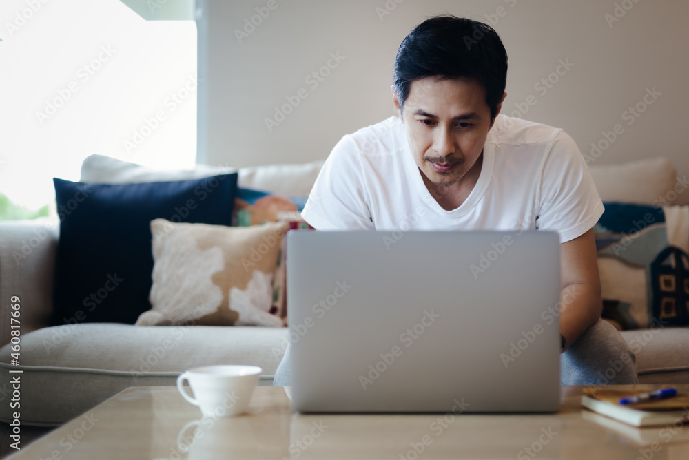 Asian businessman sits in a couch at home working on laptop. Asian businessman sits in a couch at home working on laptop.