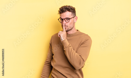 young handsome hispanic man asking for silence and quiet, gesturing with finger in front of mouth, saying shh or keeping a secret photo