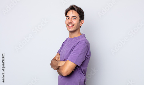 young handsome hispanic man smiling to camera with crossed arms and a happy, confident, satisfied expression, lateral view