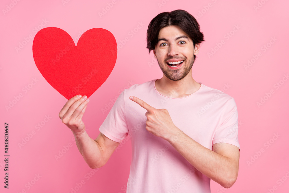 Photo portrait man pointing finger paper heart postcard isolated pastel pink color background Photo portrait man pointing finger paper heart postcard isolated pastel pink color background