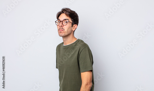 фотография young handsome hispanic man with a goofy, crazy, surprised expression, puffing c