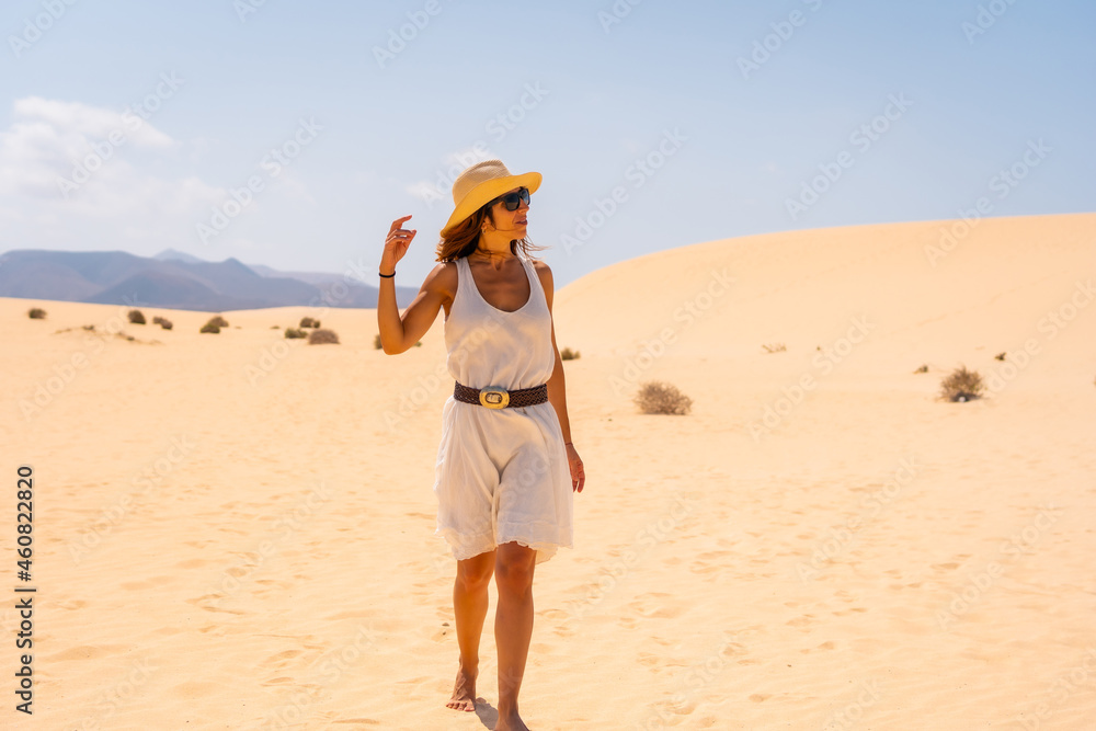 A young European tourist wearing a hat walking through the dunes of the Corralejo Natural Park, Fuerteventura, Canary Islands. Spain
