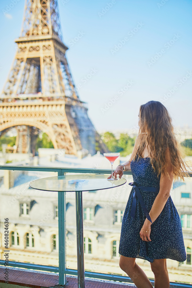 Young woman drinking alcoholic cocktail in a rooftop restaurant with view to the Eiffel tower in Paris, France