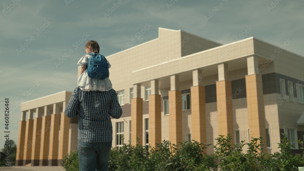 dad carries a little daughter on his shoulders to school, a girl with a school bag on his shoulders, walk around the schoolyard, see off to first grade, preschool education, father day, happy family