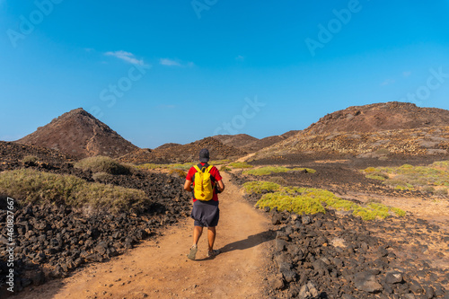 A young man with a yellow backpack on the trail heading north to Isla de Lobos, along the north coast of the island of Fuerteventura, Canary Islands. Spain