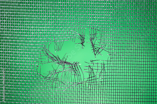 Torn window screen against green background, closeup