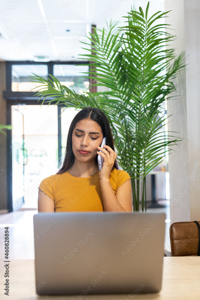 Busy woman talking on smartphone and using laptop