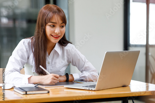 Portrait of Asian Young female freelancer is working her job on computer tablet in modern office. Doing accounting analysis report real estate investment data, Financial and tax systems concept.