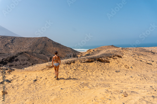 A young woman on a path of the wild beach Cofete of the natural park of Jandia, Barlovento coast, south of Fuerteventura, Canary Islands. Spain