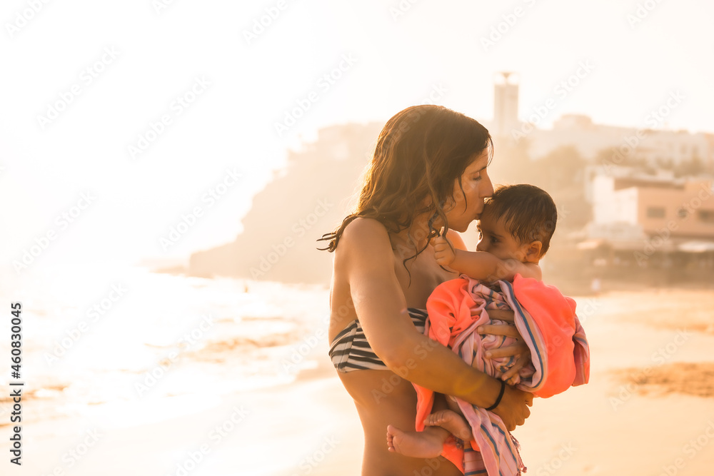 Fototapeta premium A mother kissing her six-month-old baby at sunset on a beach, Morro Jable, Municipality of Pajara south of Fuerteventura, Canary Islands. Spain