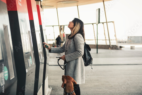 Young woman with dog paying through credit card while buying ticket at station photo