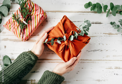 Furoshiki tissue wrapping of presents. Female hand holding a gift in eco friendly reusable fabric package. Small business, ethical shopping idea. Presents packed in plastic free. Zero waste lifestyle photo