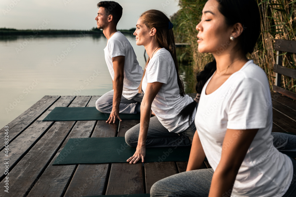 Group of people doing yoga exercises by the lake at sunset.	