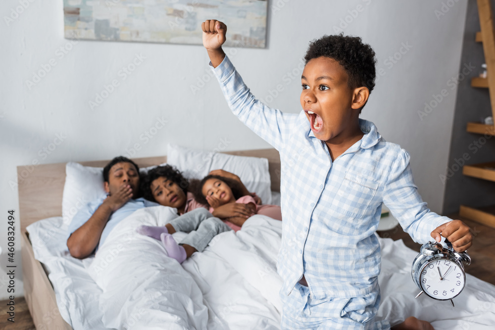 excited african american boy with alarm clock screaming and showing