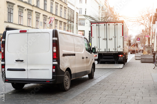 Fototapeta Naklejka Na Ścianę i Meble -  Small white van and mid size cargo truck parked for unloading at european old city street road. Fast express courier delivery service concept. Moving and orders shipping logistics distribution