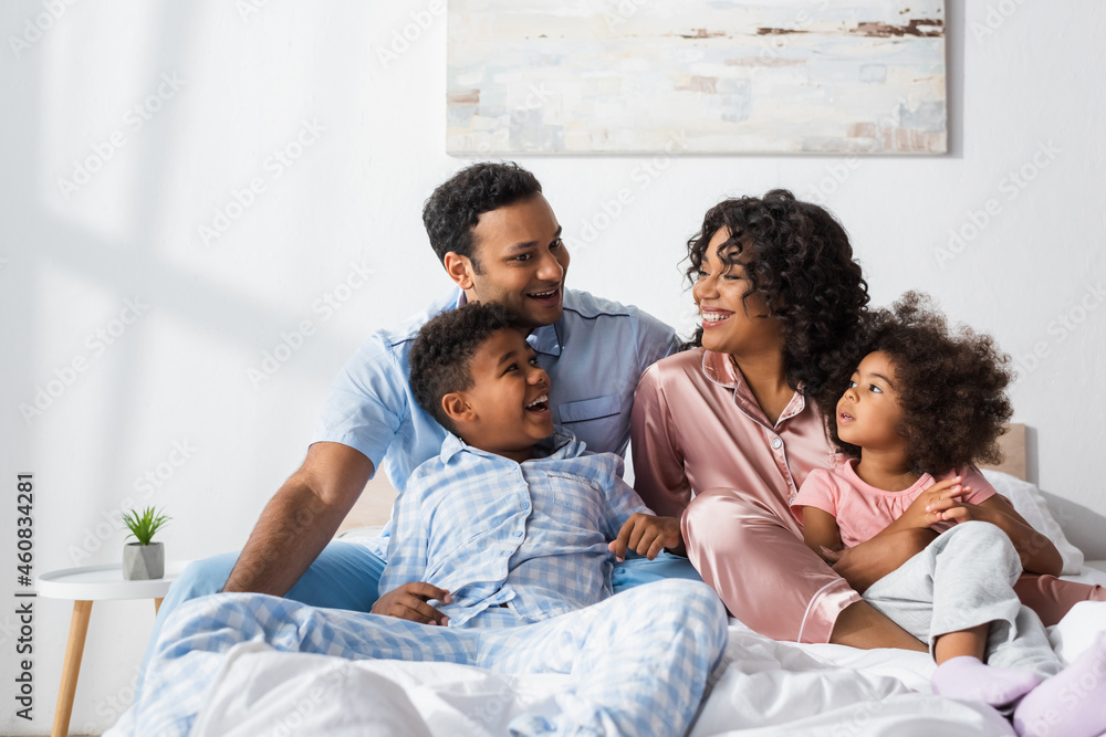 happy african american couple talking in bed near cheerful kids happy african american couple talking in bed near cheerful kids