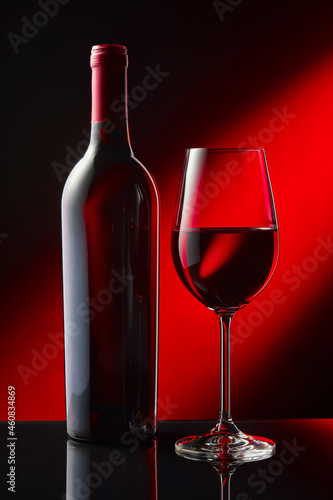 A bottle and a glass of red wine stand on a black mirror table.