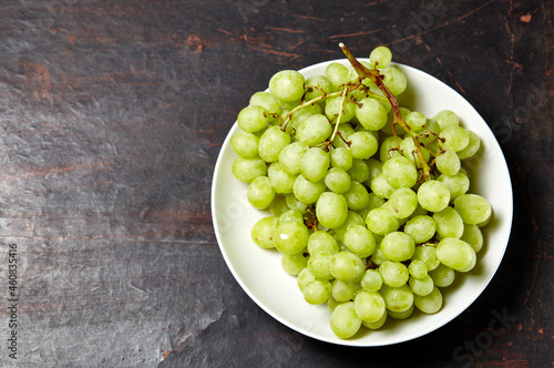 Branch of ripe green grape on plate with water drops. Juicy grapes on wooden background, closeup. Grapes on dark kitchen table with copy space