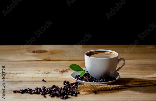 Hot cappuccino coffee in cup and beans with green leaf on wooden table at cafe. Dark scene and use for banner