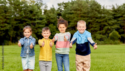 childhood, leisure and people concept - multiethnic group of happy kids showing thumbs up at park