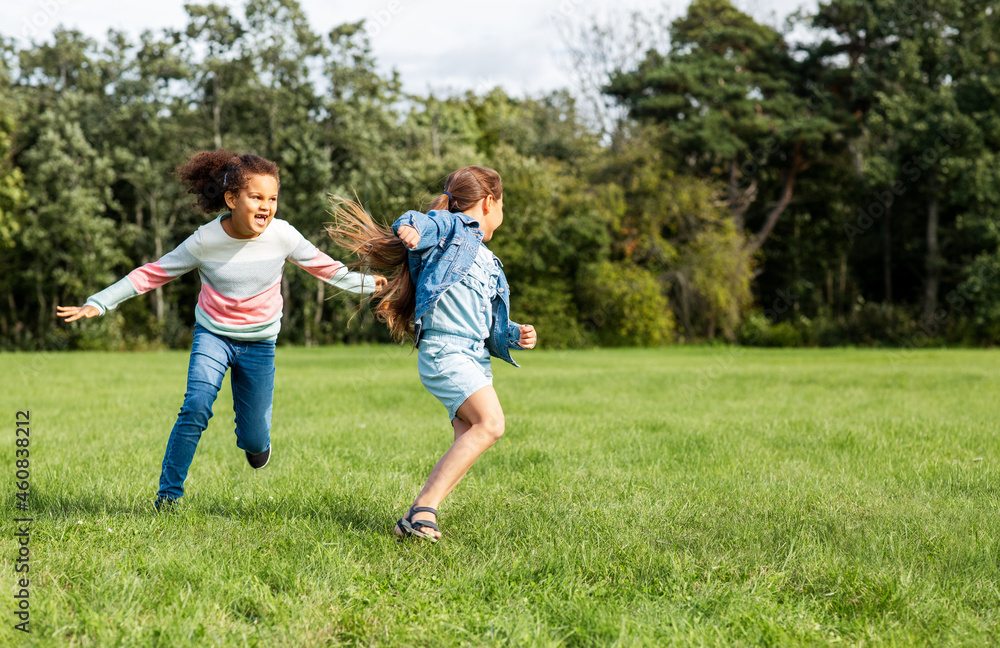 childhood, leisure and people concept - happy girls playing tag game and running at park