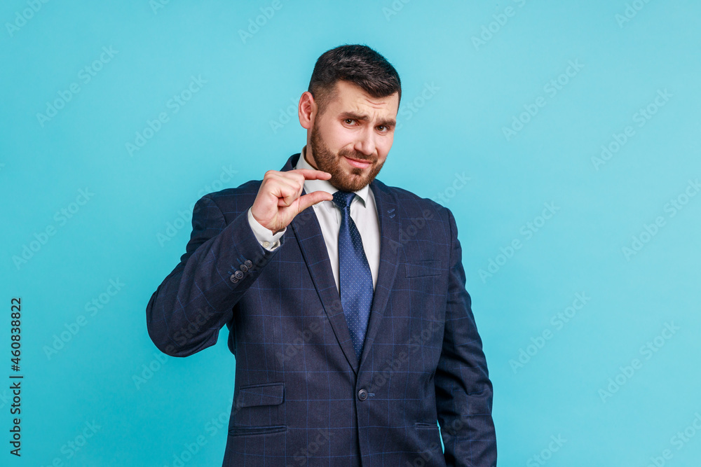 Handsome bearded businessman wearing official style suit showing a little bit gesture, small amount or low scale sign, few centimeters. Indoor studio shot isolated on blue background. Handsome bearded businessman wearing official style suit showing a little bit gesture, small amount or low scale sign, few centimeters. Indoor studio shot isolated on blue background.
