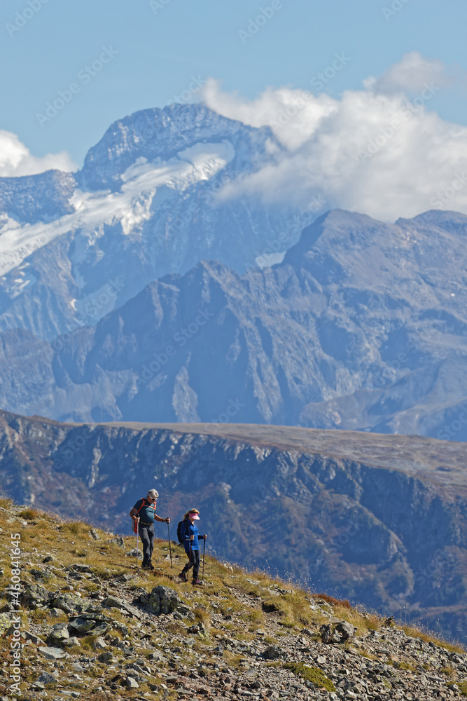 CHAMROUSSE, FRANCE, September 23, 2021 : Couple of hikers on the slopes, with high snowy summit in the background