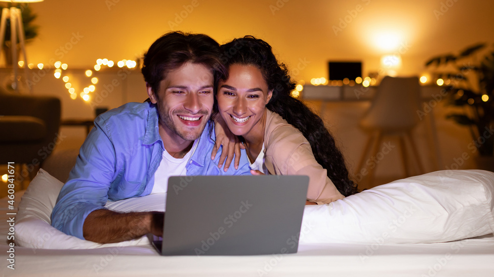 Spouses Watching Film On Laptop Lying In Bed At Home Spouses Watching Film On Laptop Lying In Bed At Home